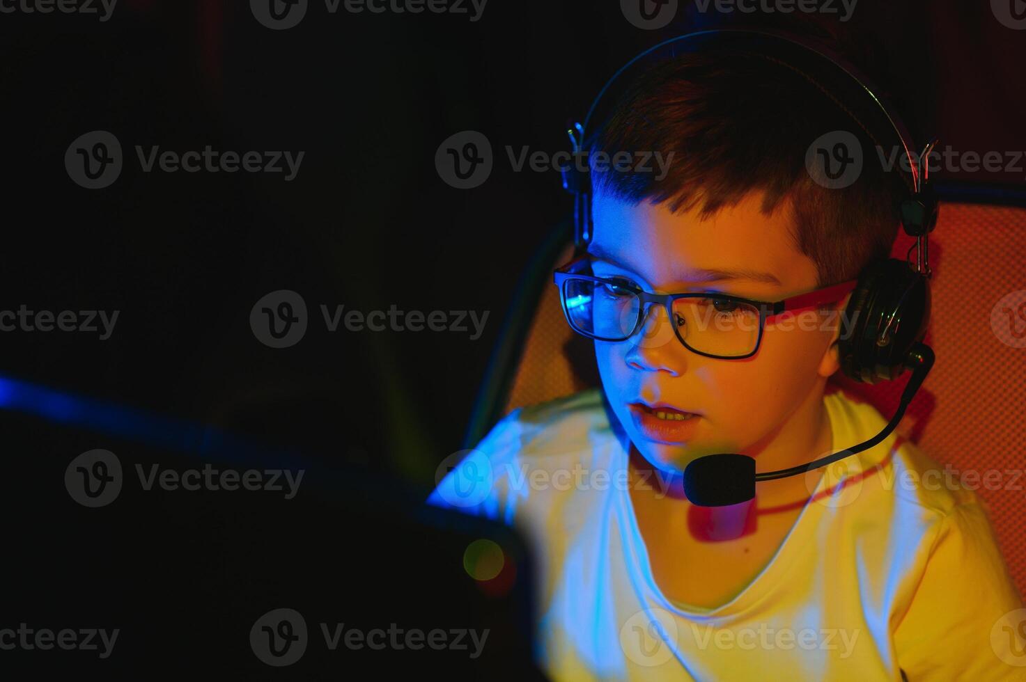 Child online broadcasts computer game, boy streams in headphones on rgb lighting background photo
