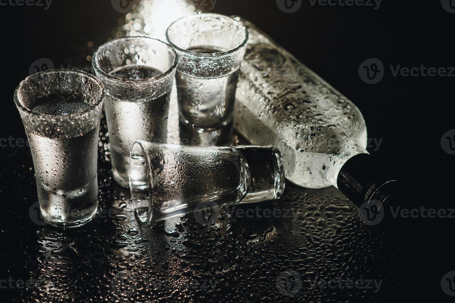 Close-up view of bottle and glasses of vodka standing isolated on black. photo