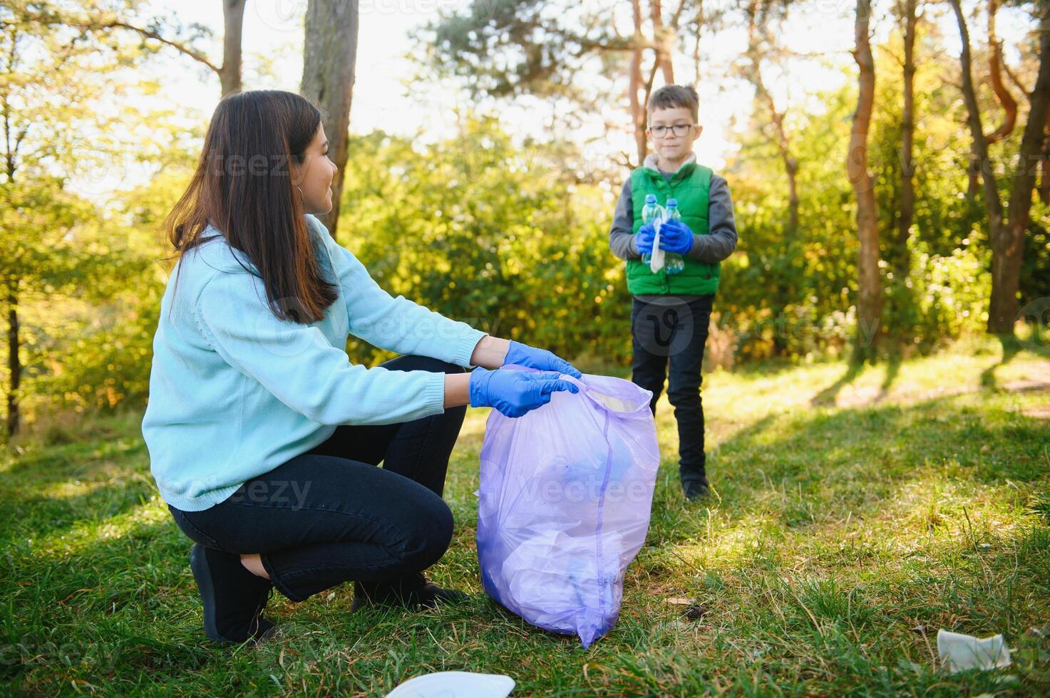 Smiling boy picking up trash in the park with his mother. Volunteer concept. photo