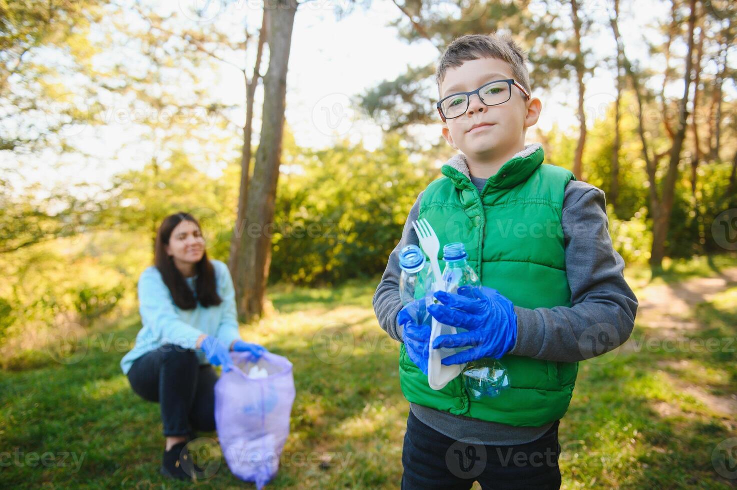 Mom teaches her son to clean up trash in nature. A woman removes plastic bottles in a bag. The topic of environmental pollution by garbage. photo