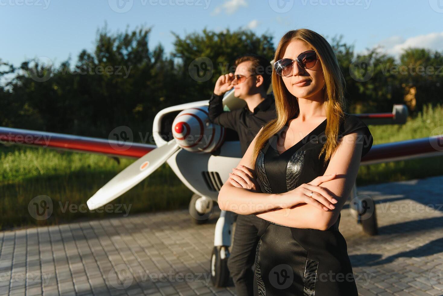 Beautiful young stylish couple in official clothes is standing near private plane. Hugging and kissing in airport in front of airplane. photo