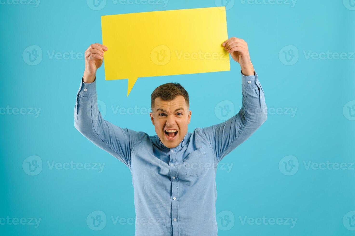 Handsome man holding blank speech bubble sign isolated on yellow studio background photo