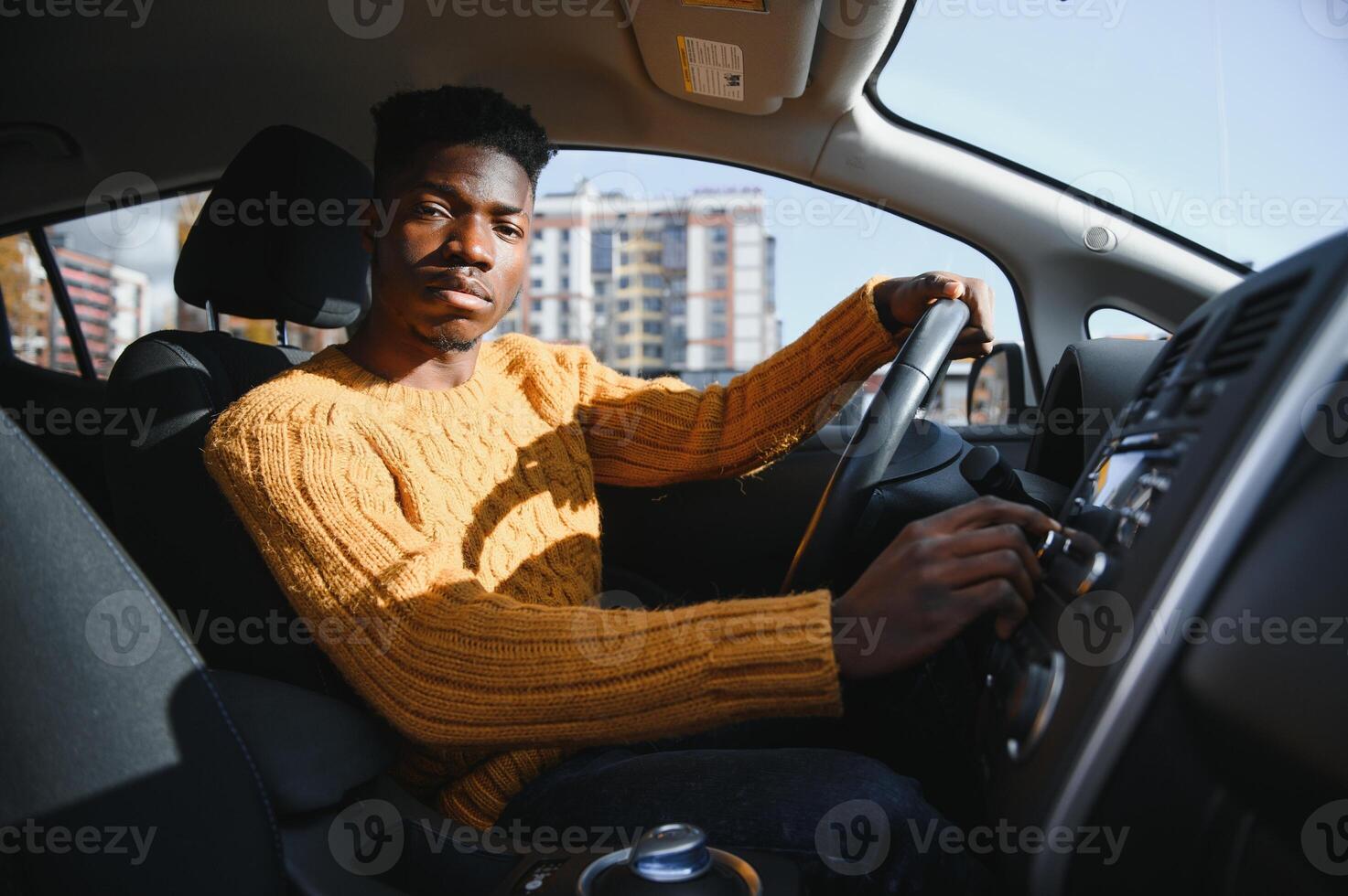 Smiling African American young man, sitting in the cabin of a comfortable modern electric car and touching the screen of navigation self-driving autopilot photo