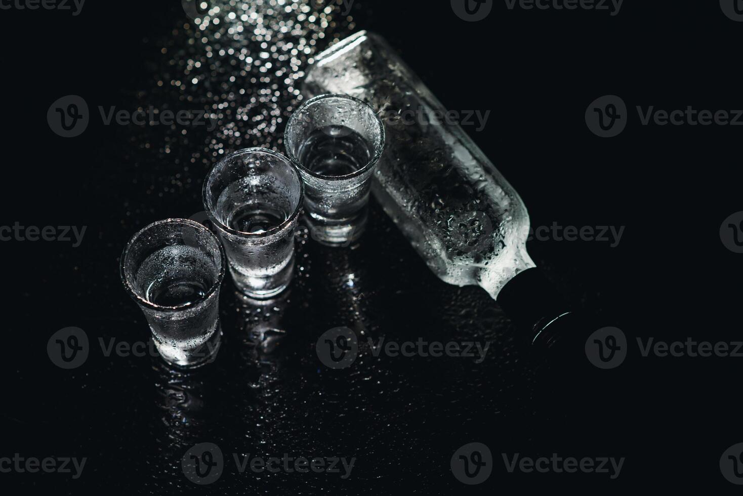 Close-up view of bottle and glasses of vodka standing isolated on black. photo