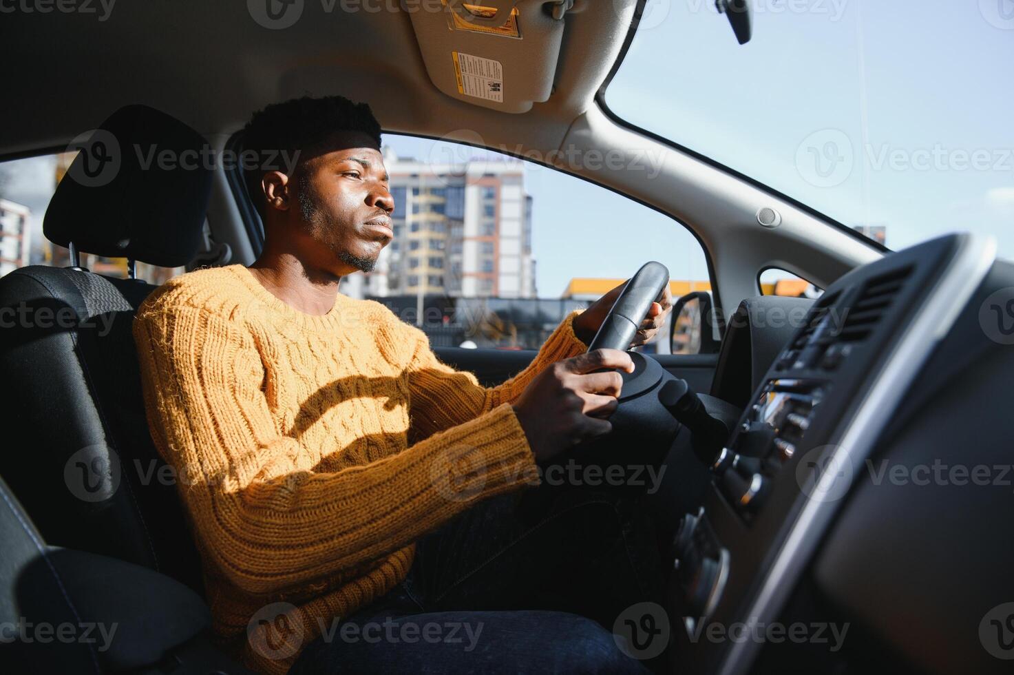 Happy smiling African American male driver sitting behind the self-driving steering wheel of an autonomous electric modern car. Happy guy holds phone and smiles to camera in modern electric car photo