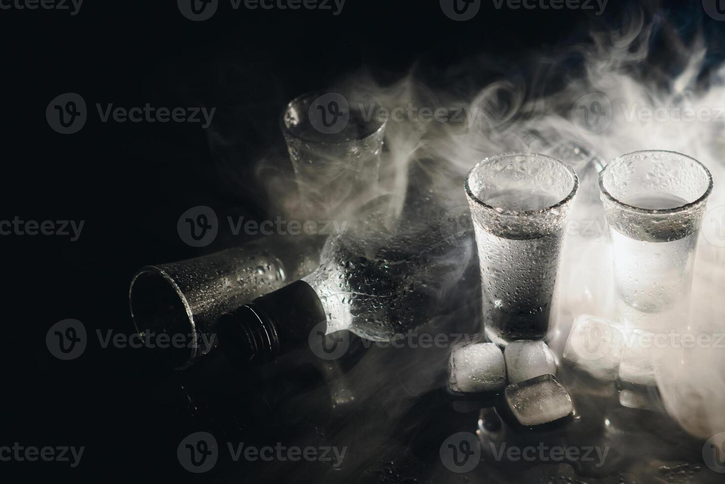 Close-up view of bottle of vodka with glasses standing on ice on black. photo