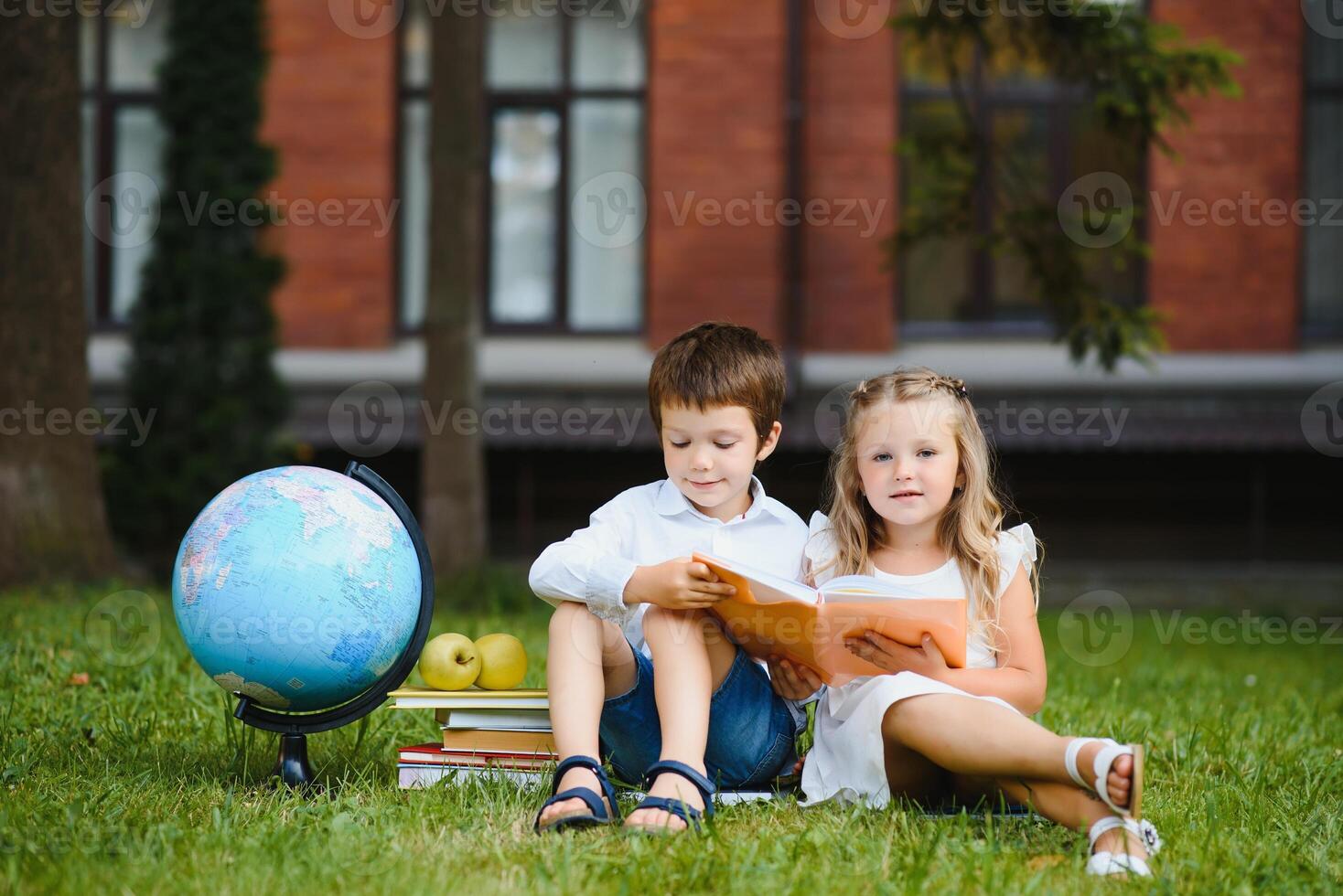 Schoolgirl sitting on green grass and talking to her friend they preparing for the lessons together before school photo