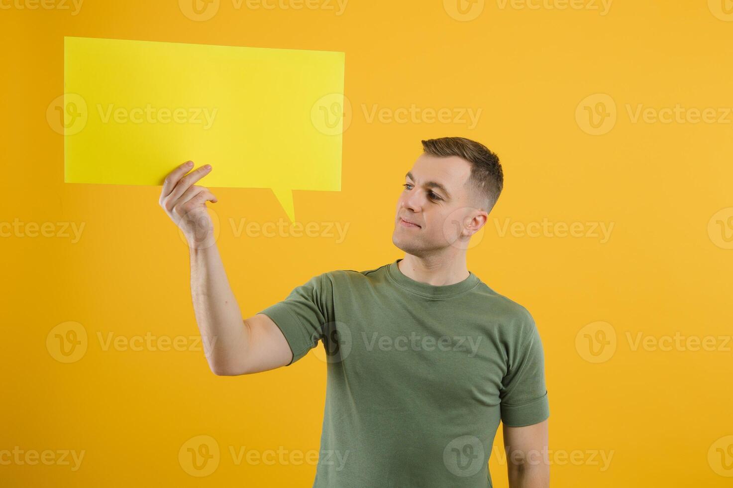 Happy guy smiling and holding blank speech balloon near head against yellow background photo