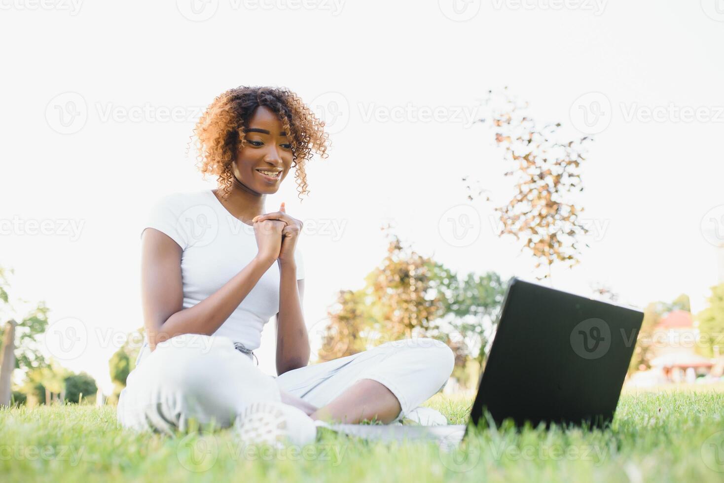 joven sonriente negro mujer sentado al aire libre en césped con computadora portátil, mecanografía, surf Internet, teniendo café. tecnología, comunicación, educación y remoto trabajando concepto, Copiar espacio foto