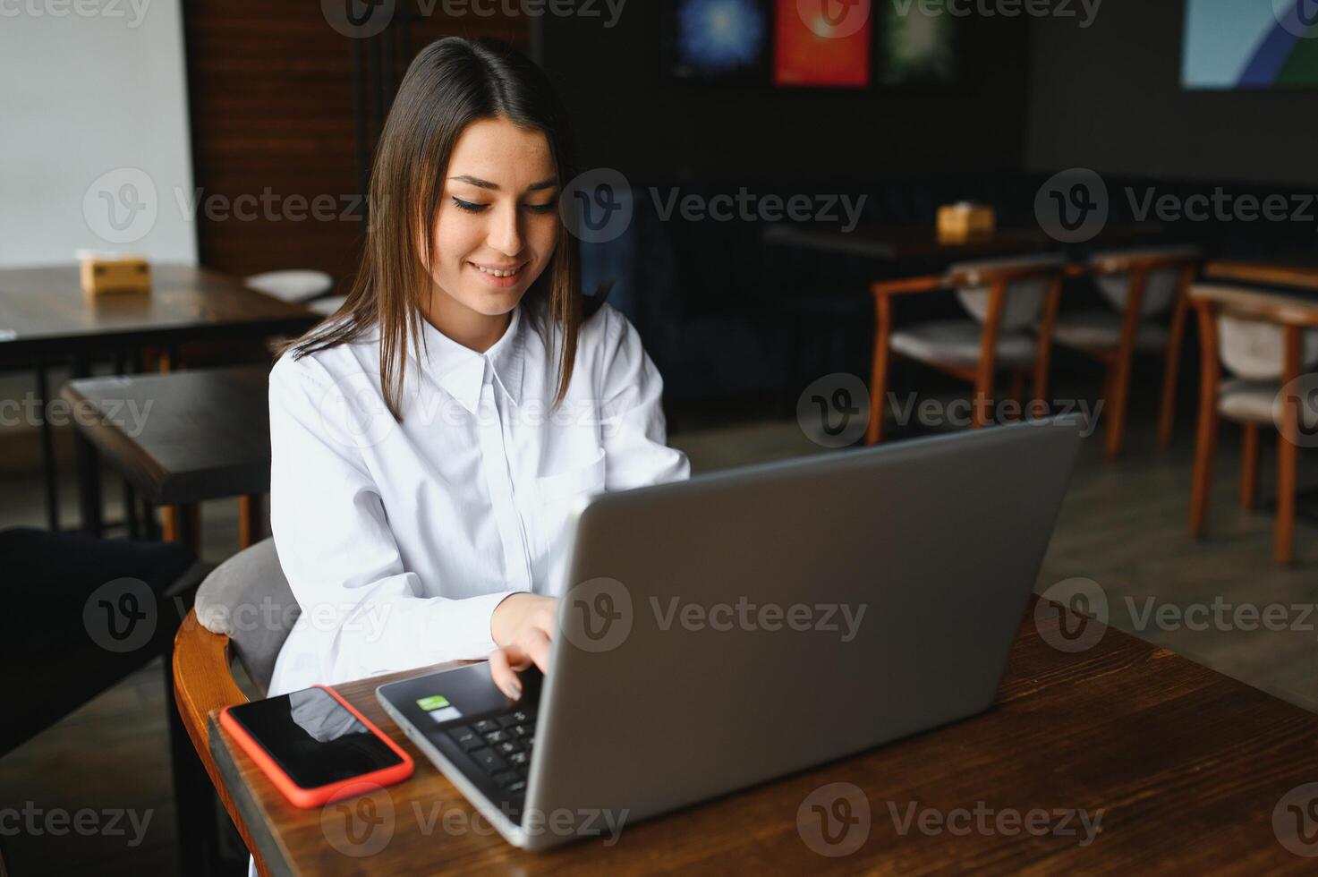 retrato de un joven hembra persona de libre dedicación utilizando ordenador portátil computadora para distancia trabajo mientras sentado en moderno café tienda interior, inteligente rubia mujer trabajando en netbook durante Mañana desayuno en café bar foto