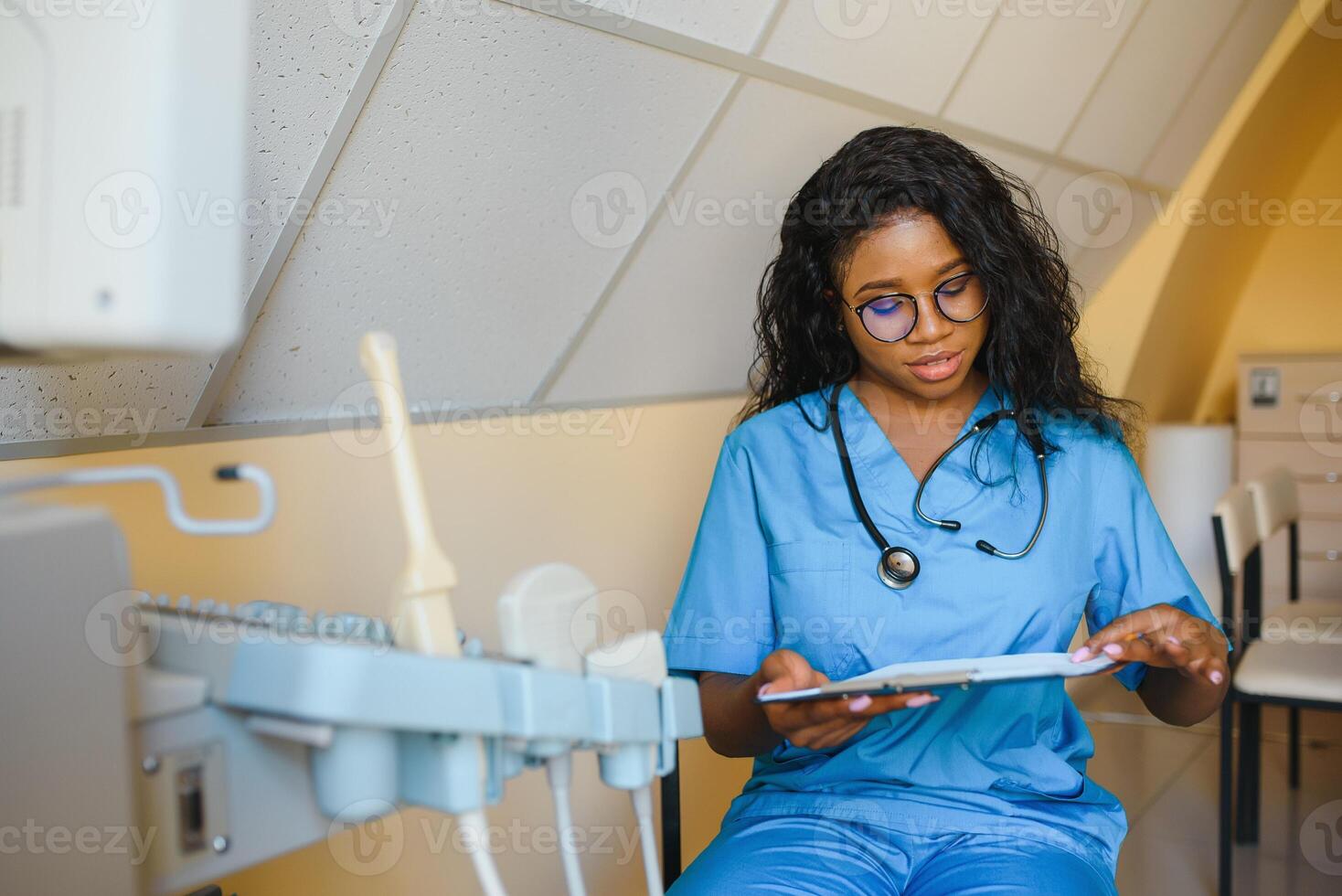 Young african american female doctor working in clinic with ultrasound machine. Records the patient's diagnosis. photo