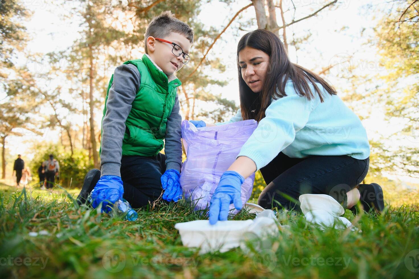 Mom teaches her son to clean up trash in nature. A woman removes plastic bottles in a bag. The topic of environmental pollution by garbage. photo