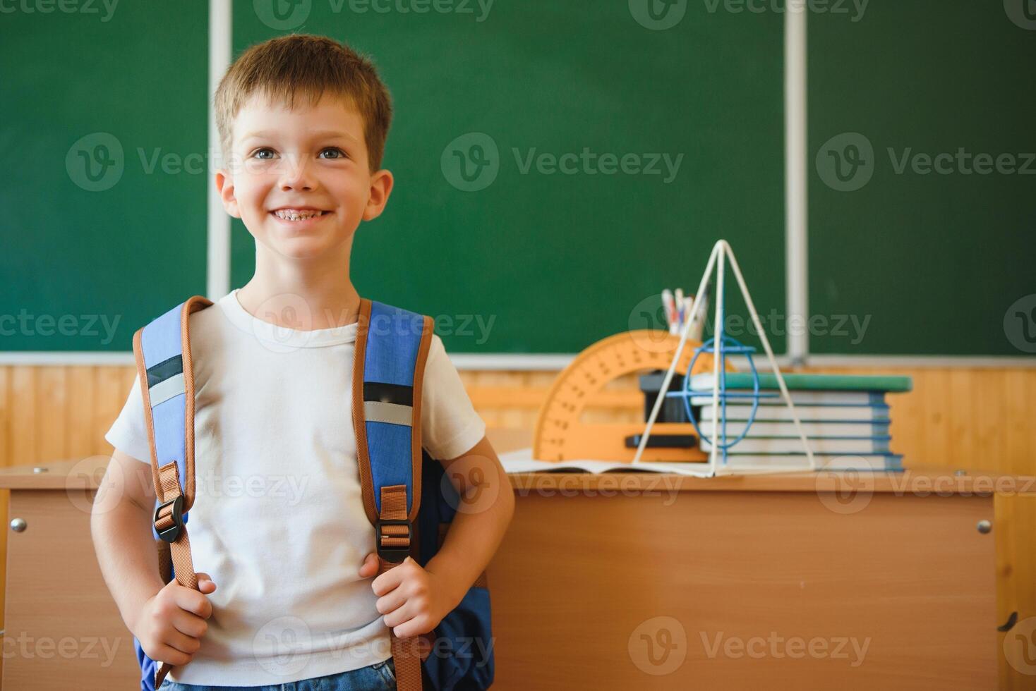 Back to school. Funny schoolboy sitting at a table with books in a school classroom. photo