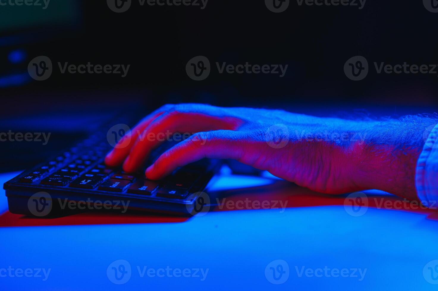 Close-up On Gamer's Hands on a keyboard, Actively Pushing Buttons, Playing MMO Games Online. Background is Lit with Neon Lights. photo