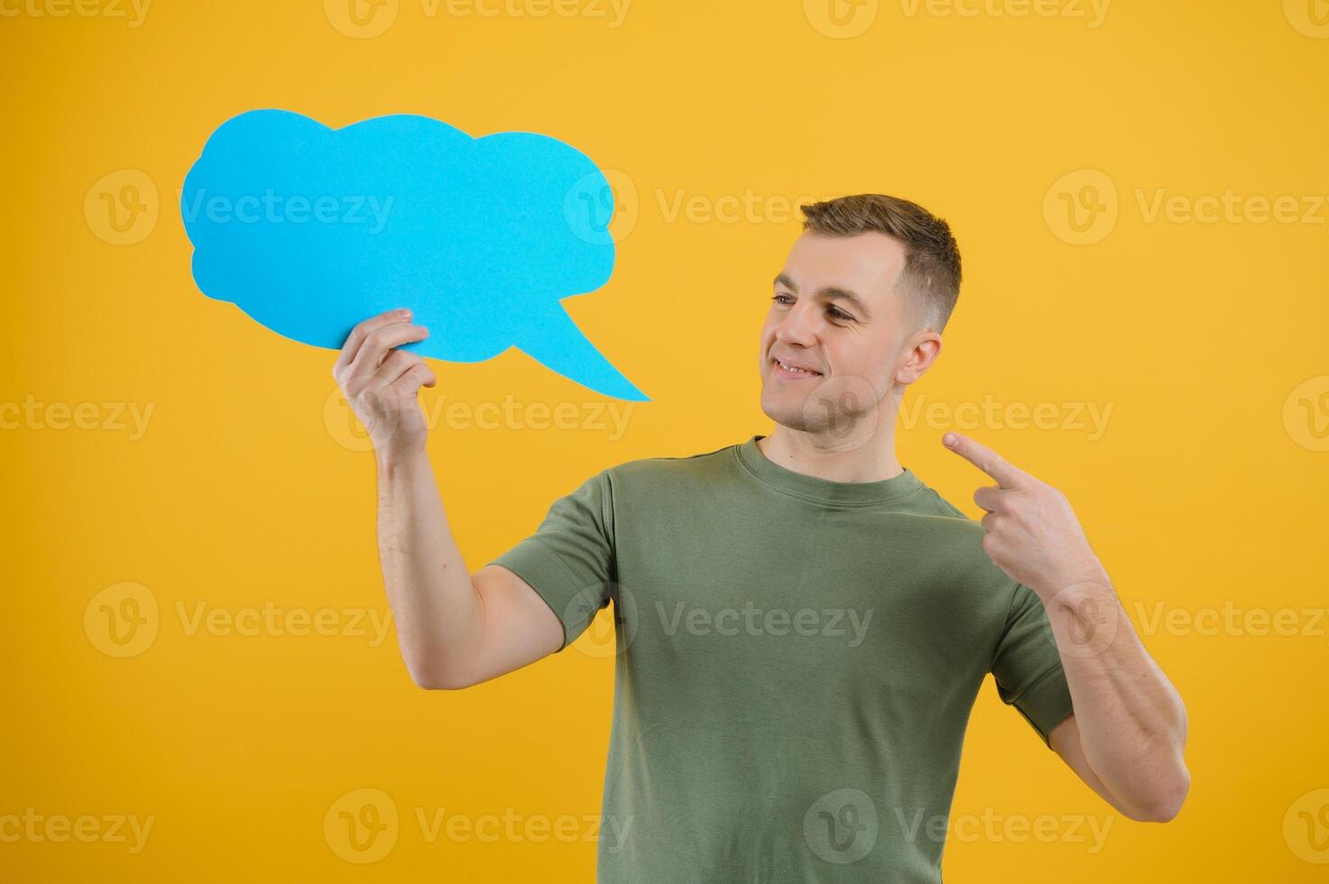 Cheerful young male pointing up and holding empty speech bubble with blank space for quote against vivid yellow background photo