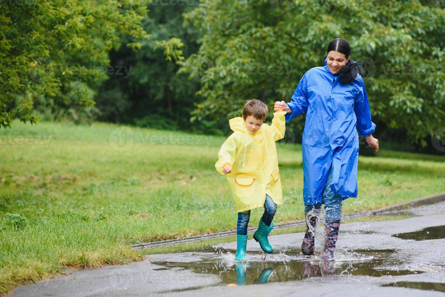 Mother and child, boy, playing in the rain, wearing boots and raincoats photo