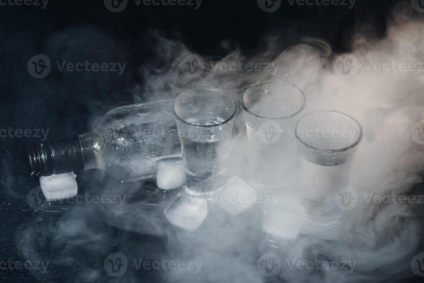 Close-up view of bottle of vodka with glasses standing on ice on black. photo