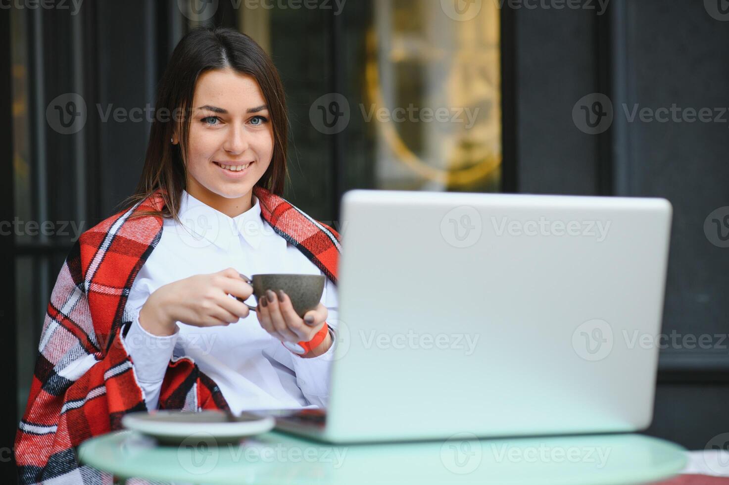 hermosa y contento mujer se sienta con un ordenador portátil en un café en el calle y bebidas café. Lanza libre trabajar. al aire libre reuniones foto