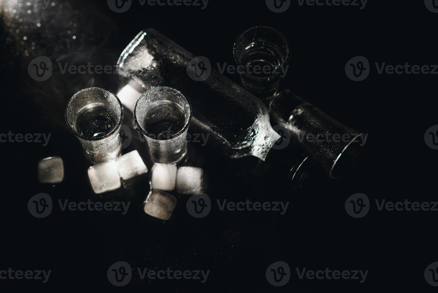 Close-up view of bottle and glasses of vodka standing isolated on black. photo