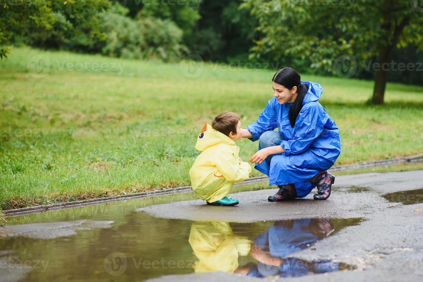 Mother and child, boy, playing in the rain, wearing boots and raincoats photo