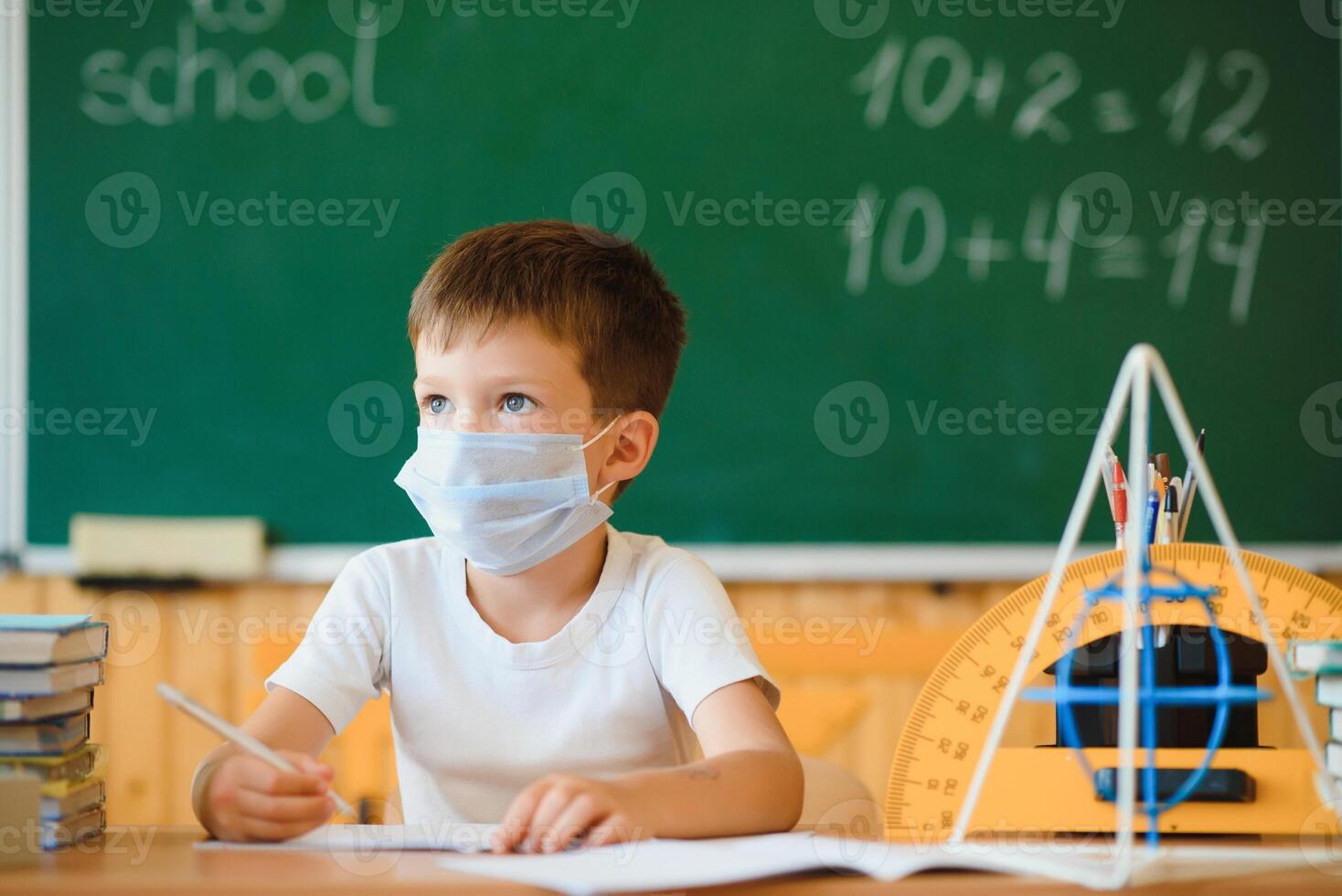 Little schoolboy wearing protective mask in classroom. Concept of epidemic photo