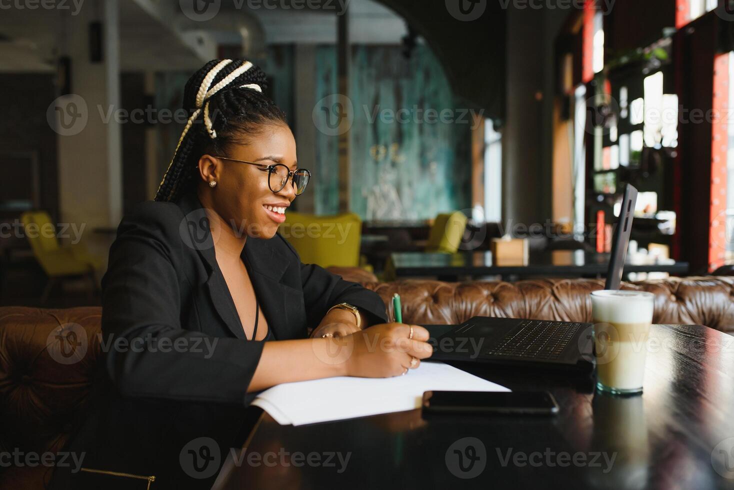 Beautiful Afro American girl in casual clothes is using a laptop and smiling while sitting in cafe photo