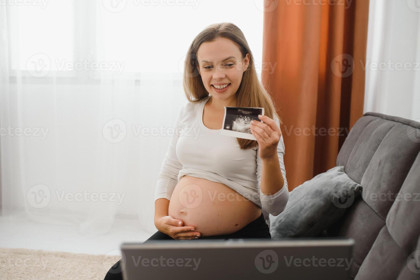 selective focus of cheerful pregnant woman showing ultrasound photos while having video call