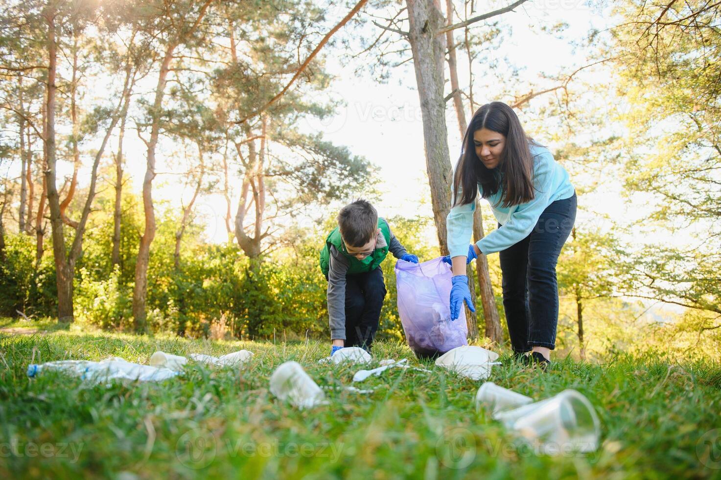 Mom teaches her son to clean up trash in nature. A woman removes plastic bottles in a bag. The topic of environmental pollution by garbage. photo