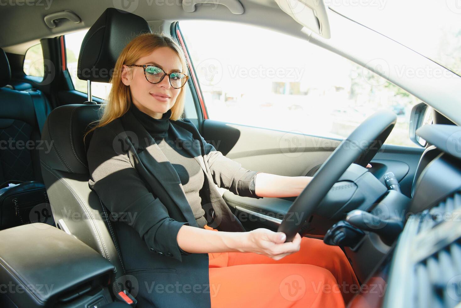 successful businesswoman driving car through modern urban city with reflections of buildings photo