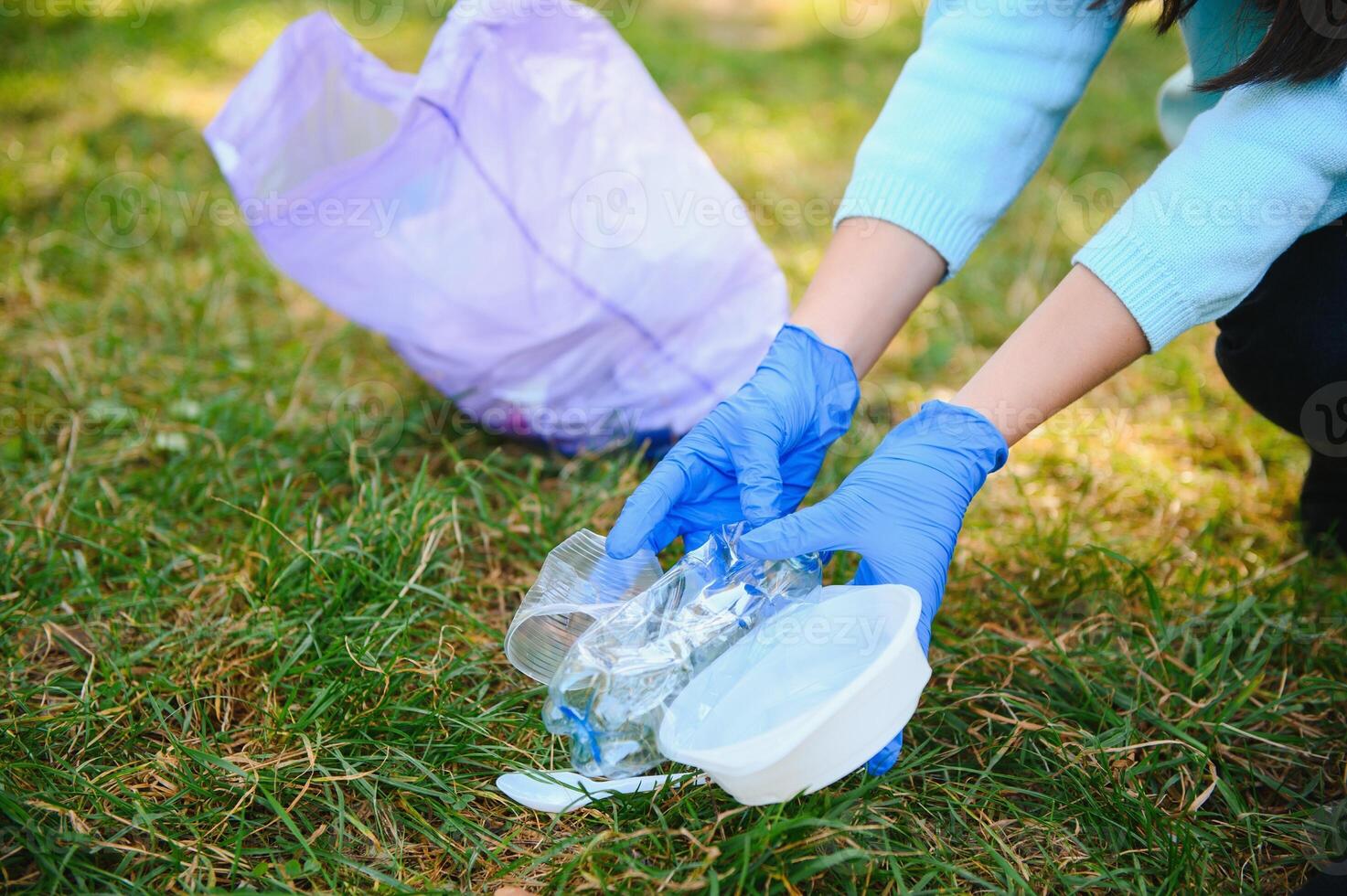 women's hands in red rubber gloves. Woman collects trash in the bag. Volunteer scavenge garbage in the summer park. Nice progressive woman making an effort to help the environment photo