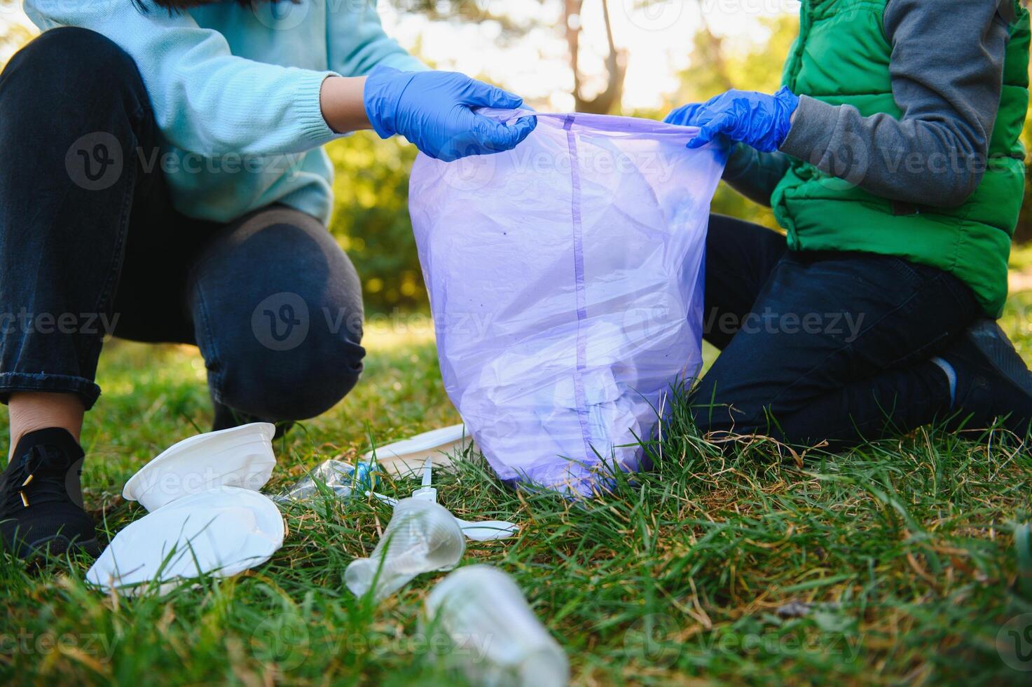 Smiling boy picking up trash in the park with his mother. Volunteer concept. photo