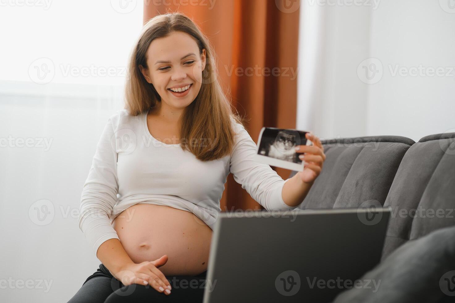 selective focus of happy pregnant woman showing ultrasound photos while having video call