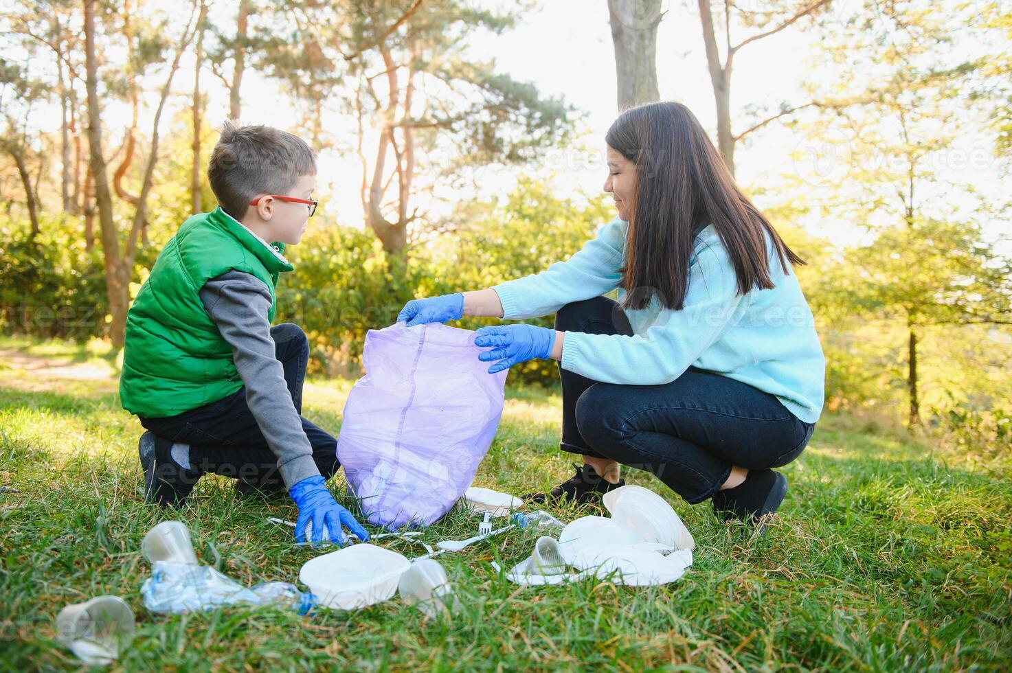 Smiling boy picking up trash in the park with his mother. Volunteer concept. photo