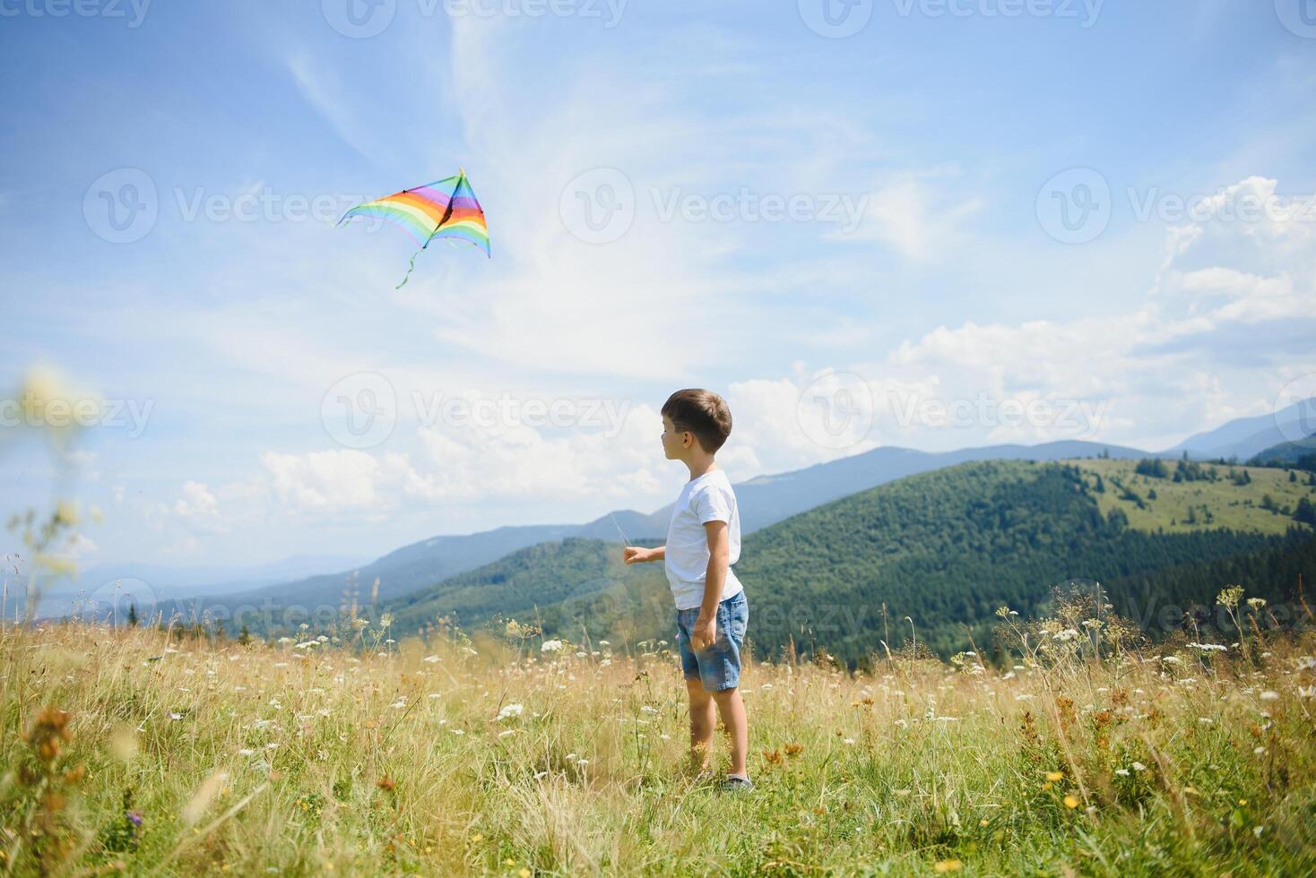 Little boy running on a background of mountains with kite. Sunny summer day. Happy childhood concept. photo