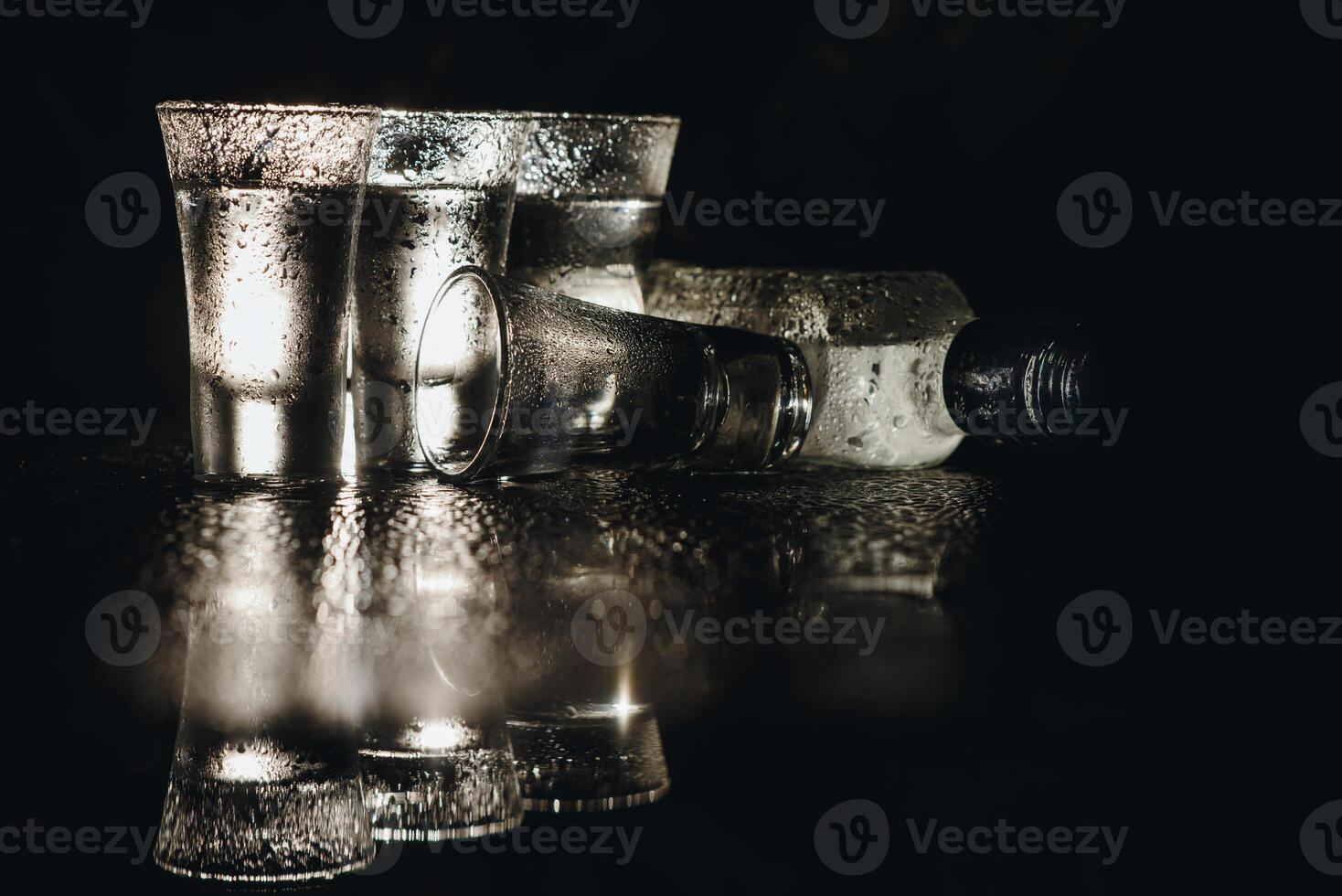 Close-up view of bottle of vodka with glasses standing on ice on black. photo