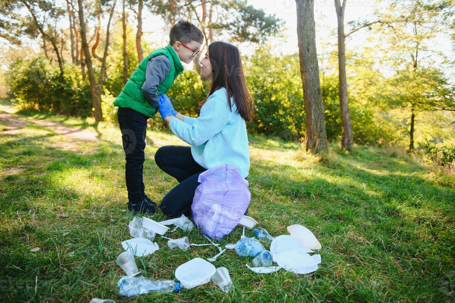 Smiling boy picking up trash in the park with his mother. Volunteer concept. photo