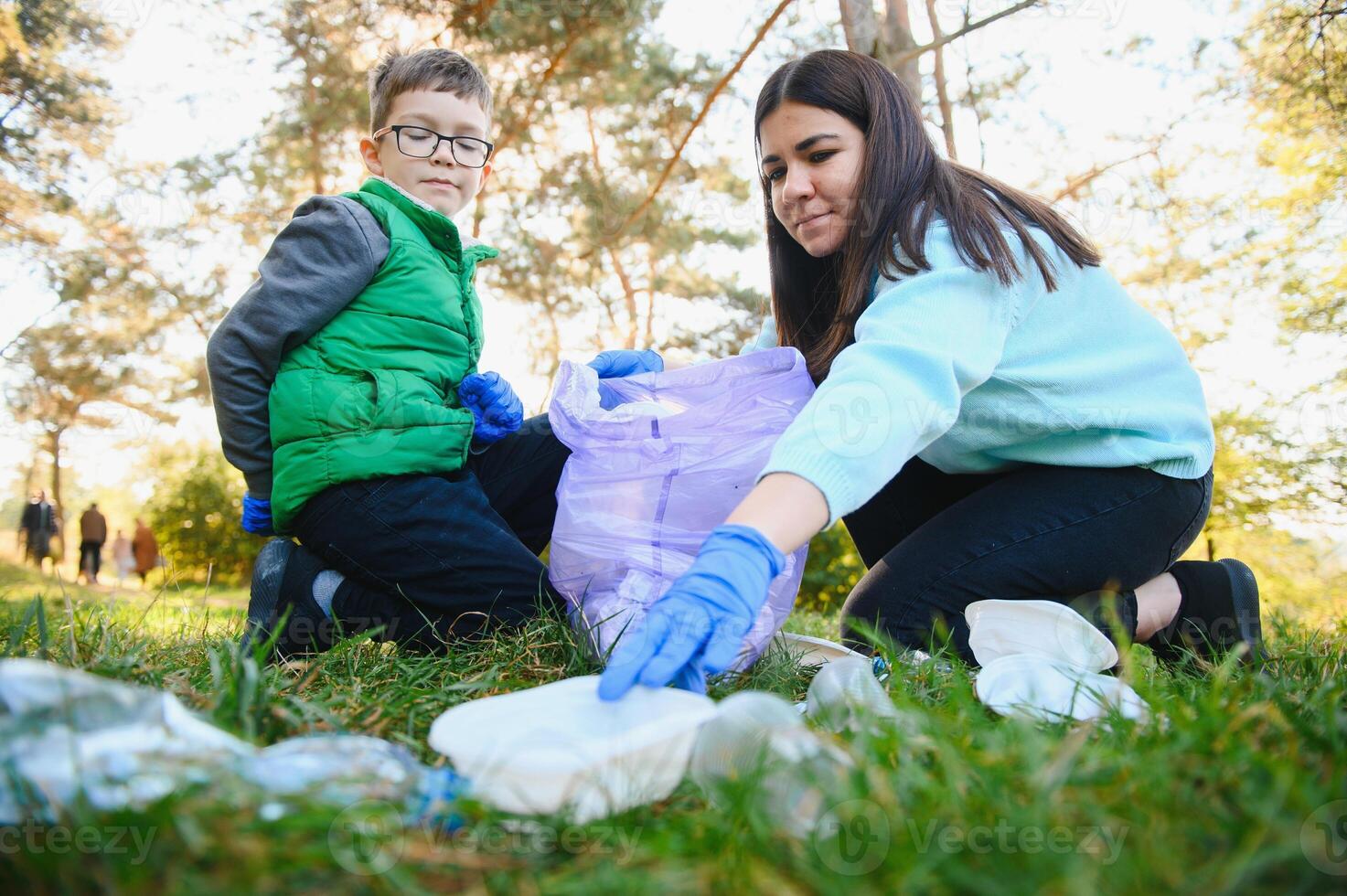 Smiling boy picking up trash in the park with his mother. Volunteer concept. photo