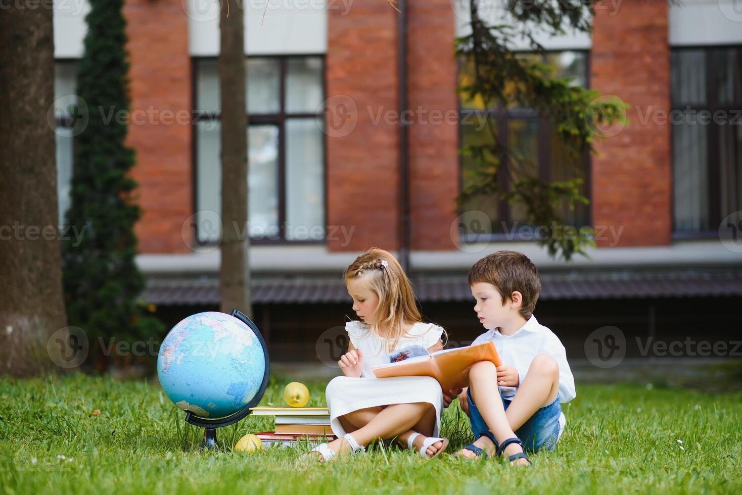 Schoolgirl sitting on green grass and talking to her friend they preparing for the lessons together before school photo