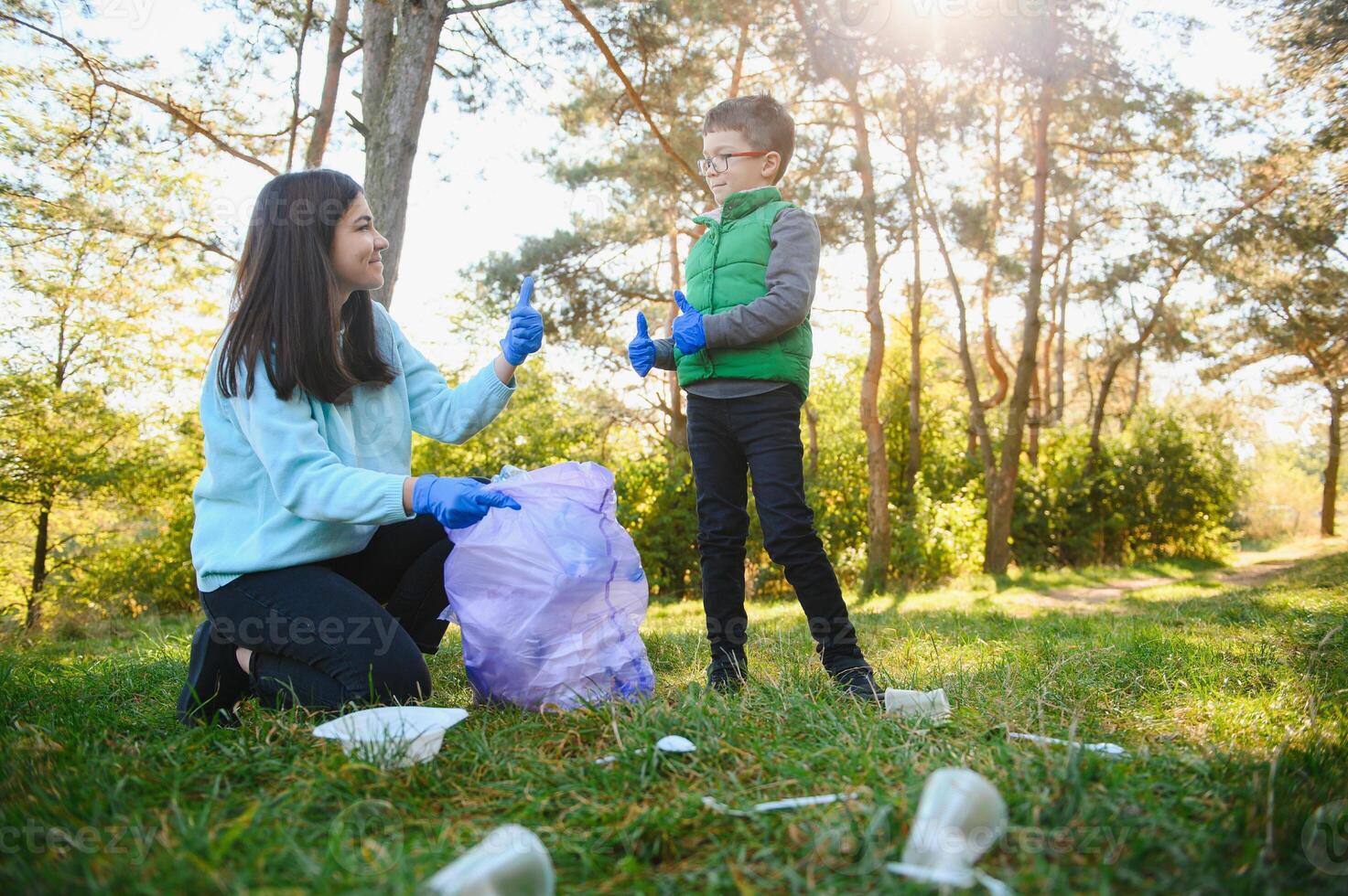 Mom teaches her son to clean up trash in nature. A woman removes plastic bottles in a bag. The topic of environmental pollution by garbage. photo