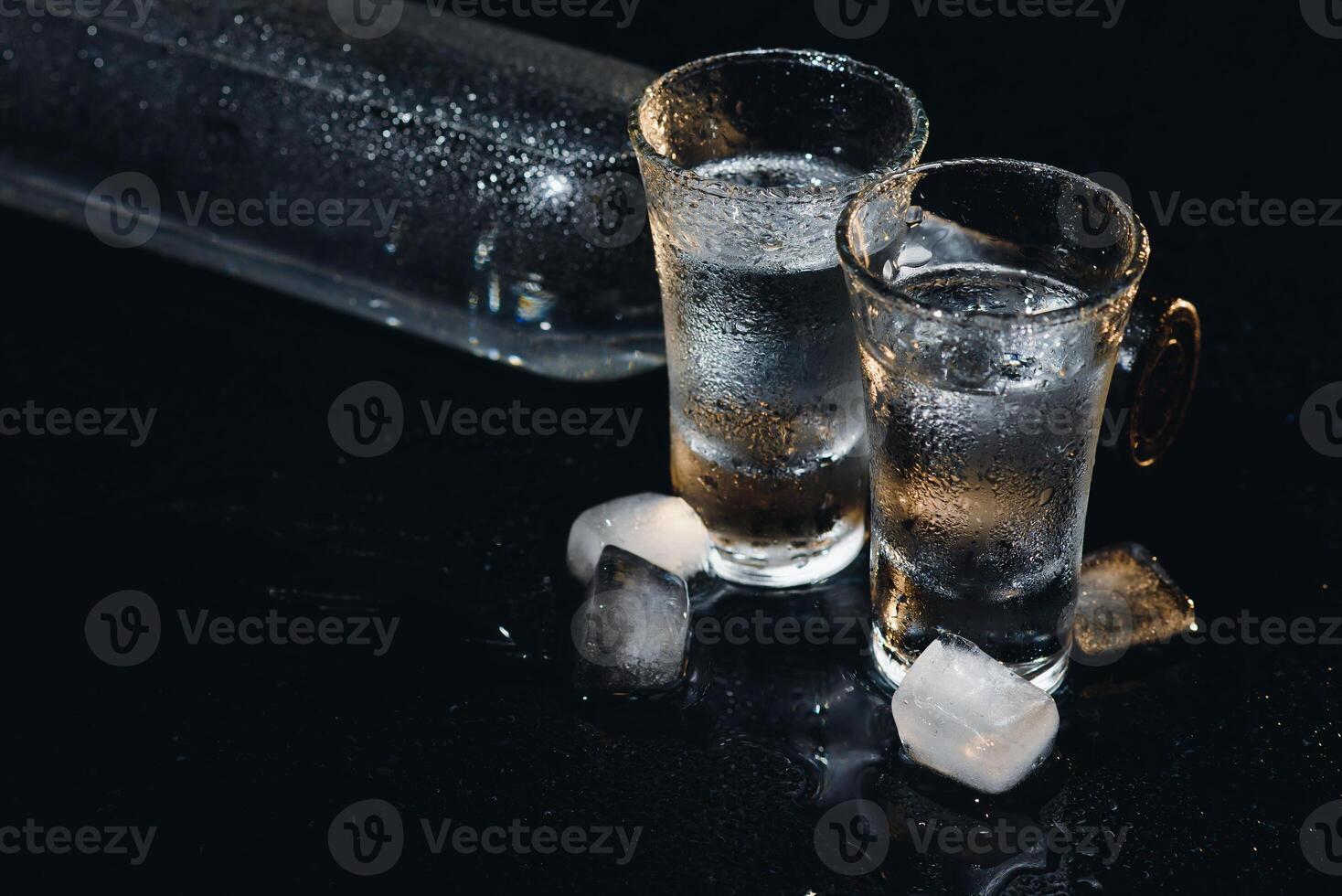 Close-up view of bottle and glasses of vodka standing isolated on black. photo
