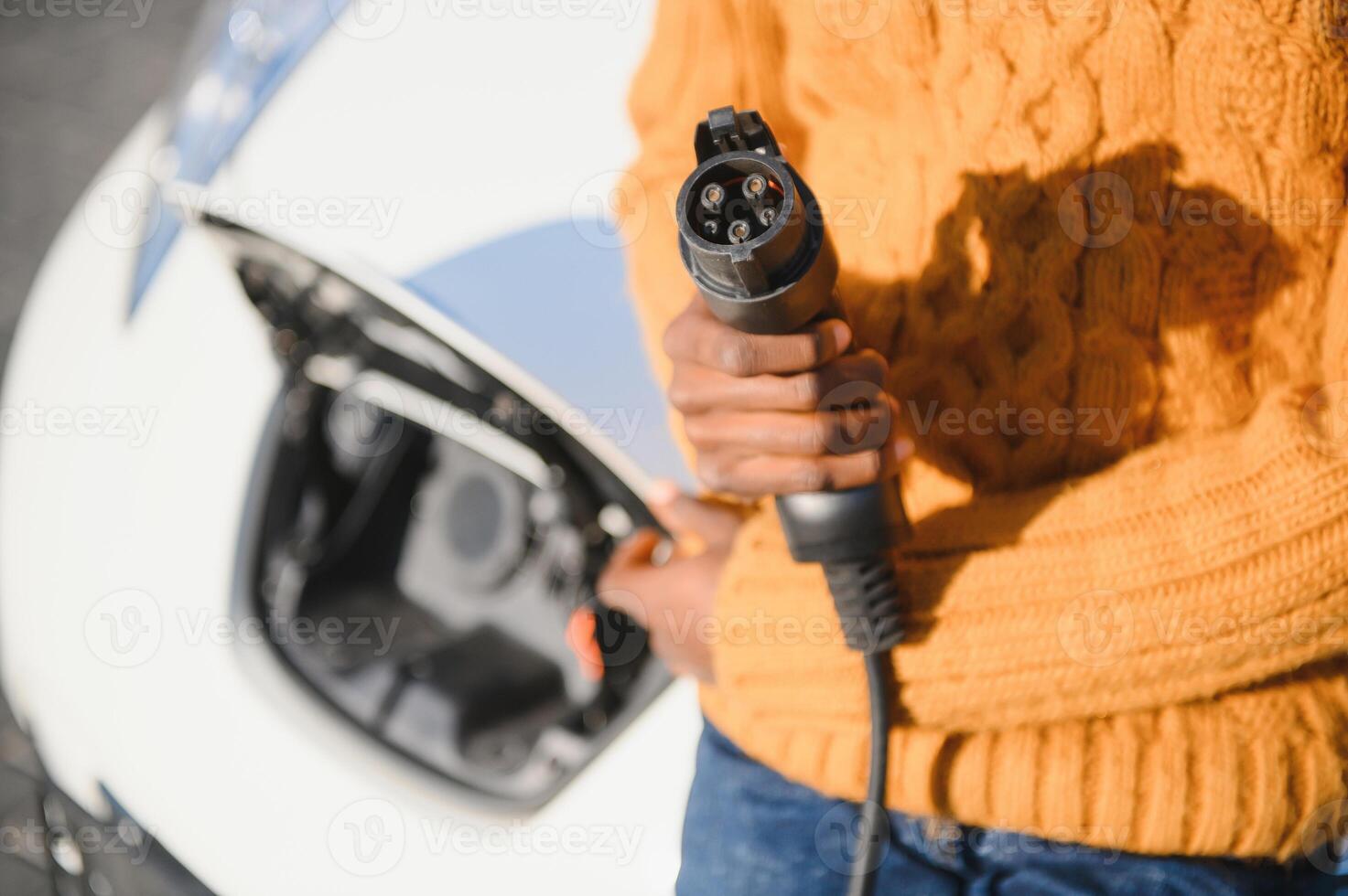 Close up of male hand holding electric charging plug for luxury red car. African businessman charging his auto on station. Eco friendly transport. photo