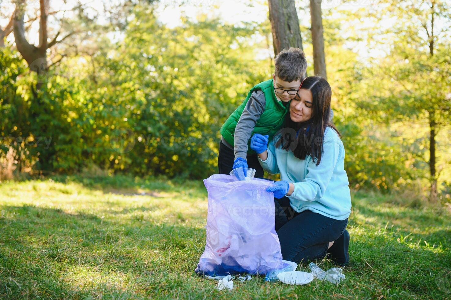 Mom teaches her son to clean up trash in nature. A woman removes plastic bottles in a bag. The topic of environmental pollution by garbage. photo