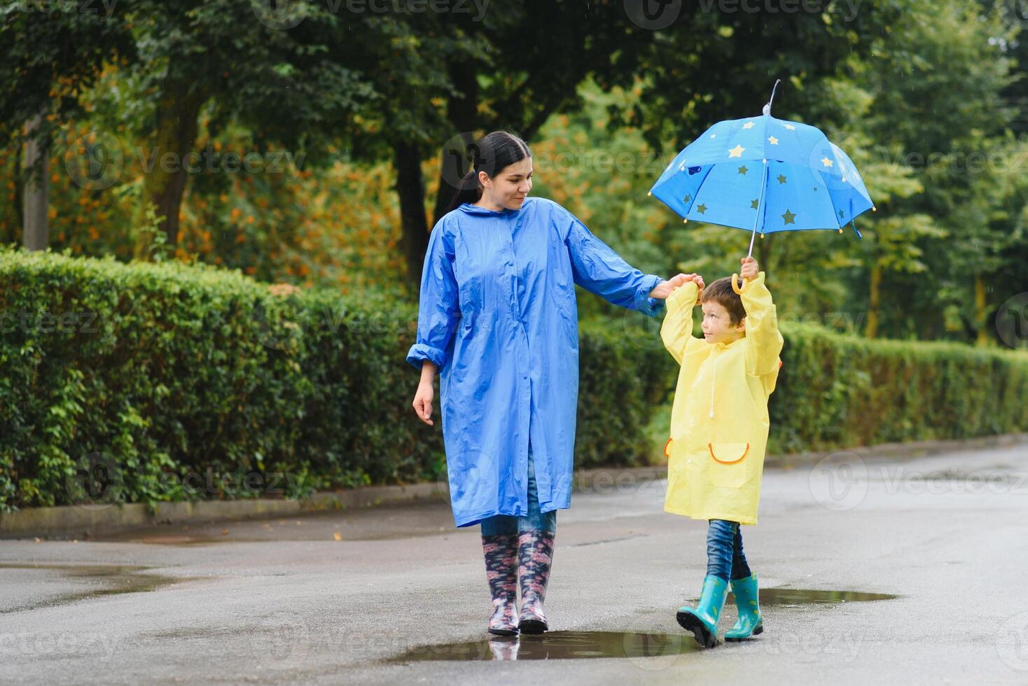 Mother and child, boy, playing in the rain, wearing boots and raincoats photo