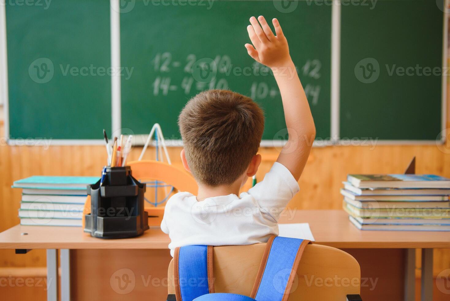 Back to school. A schoolboy is reading a book while sitting at the table for the first time at school on the background of the school blackboard. photo