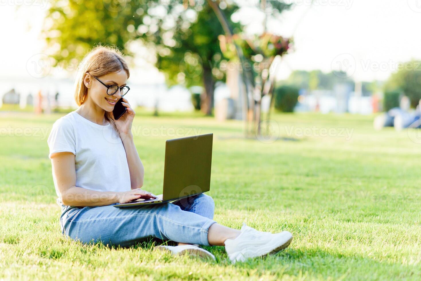 beautiful woman working with laptop in the park on the grass. The concept of remote work photo