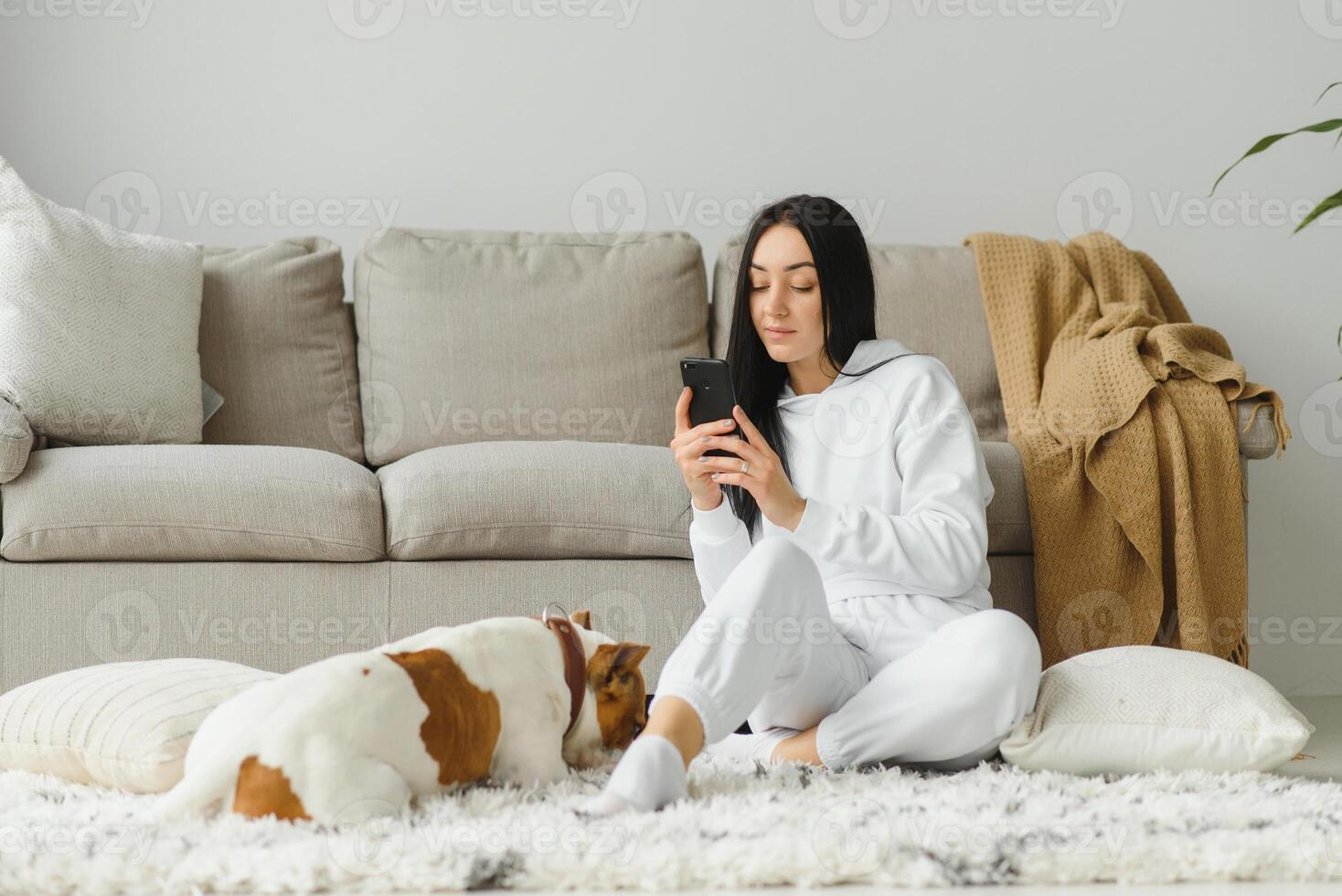 Portrait of beautiful young woman with her dog using mobile phone at home photo
