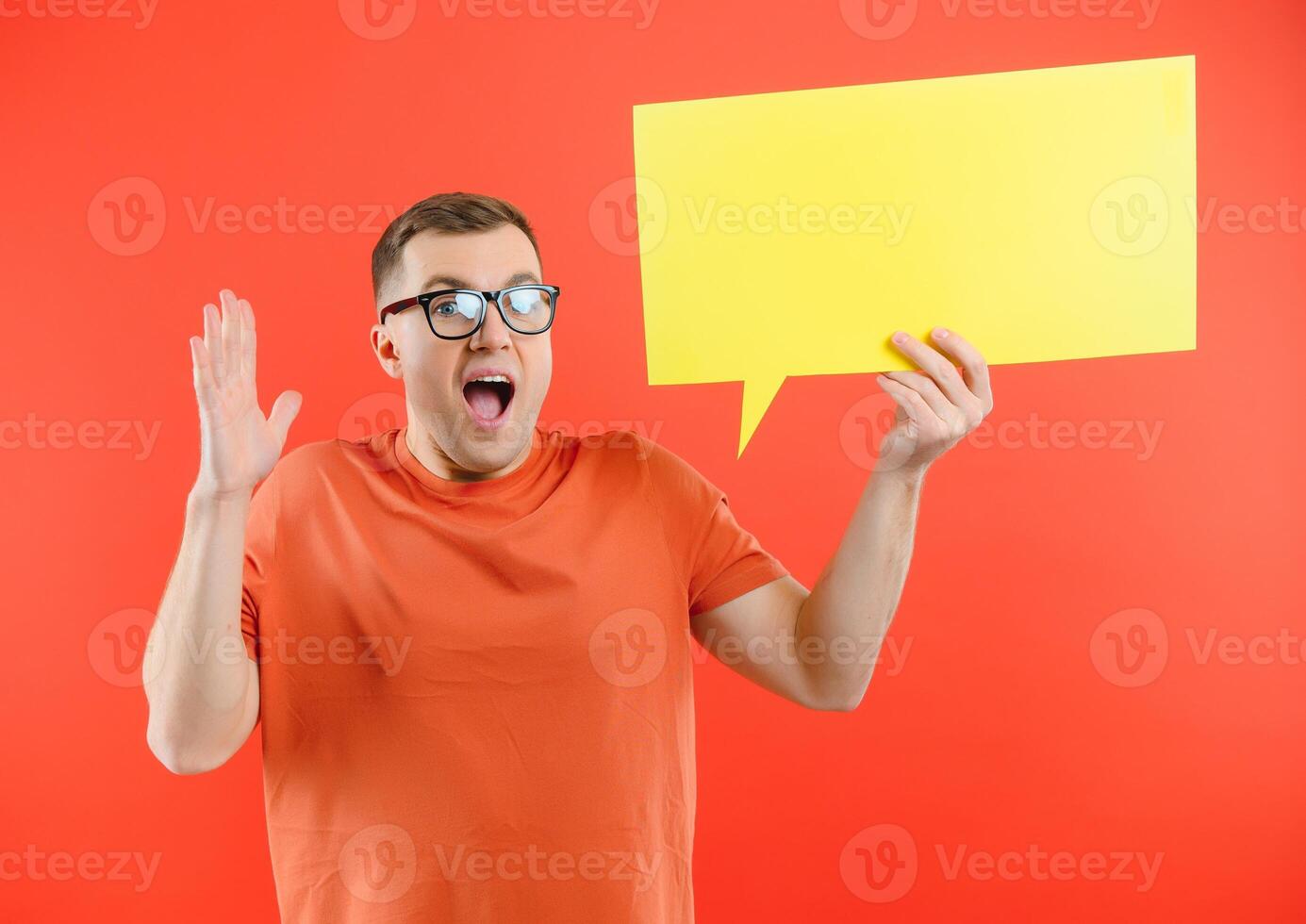 Happy smiling man holding yellow bubble speech, looking at camera over red background photo