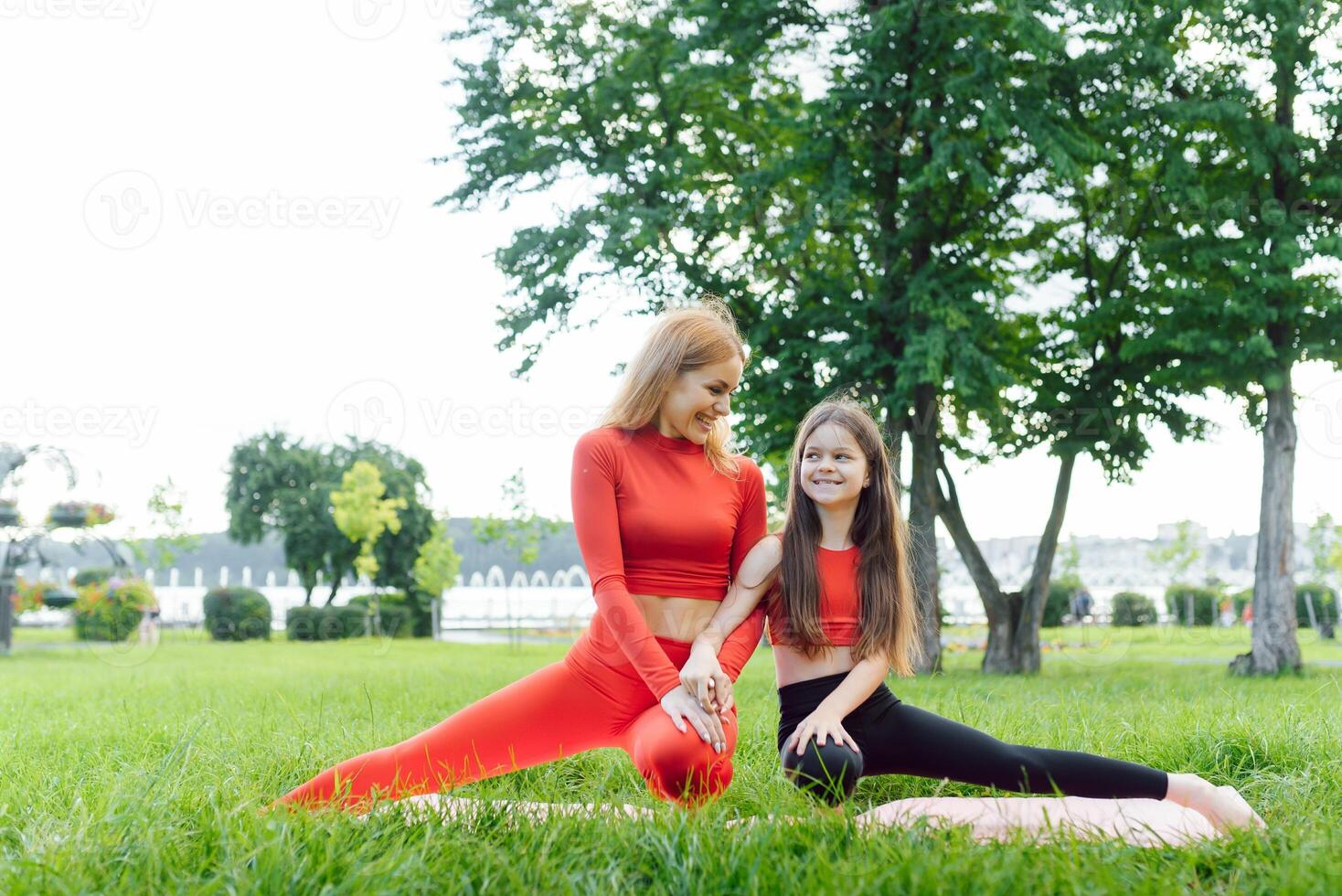 Mother and daughter doing yoga exercises on grass in the park at the day time photo