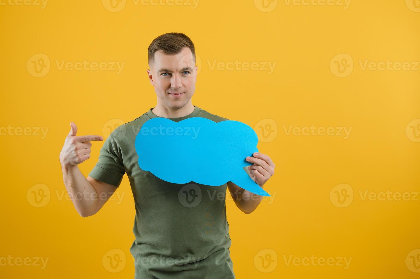 Handsome man holding blank speech bubble sign isolated on yellow studio background photo