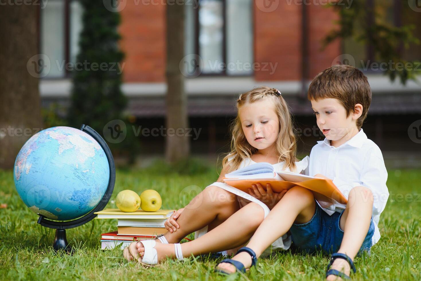 Schoolgirl sitting on green grass and talking to her friend they preparing for the lessons together before school photo